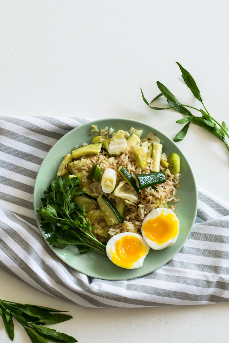 A top view of a healthy vegetable rice dish with soft-boiled eggs on a light green plate.