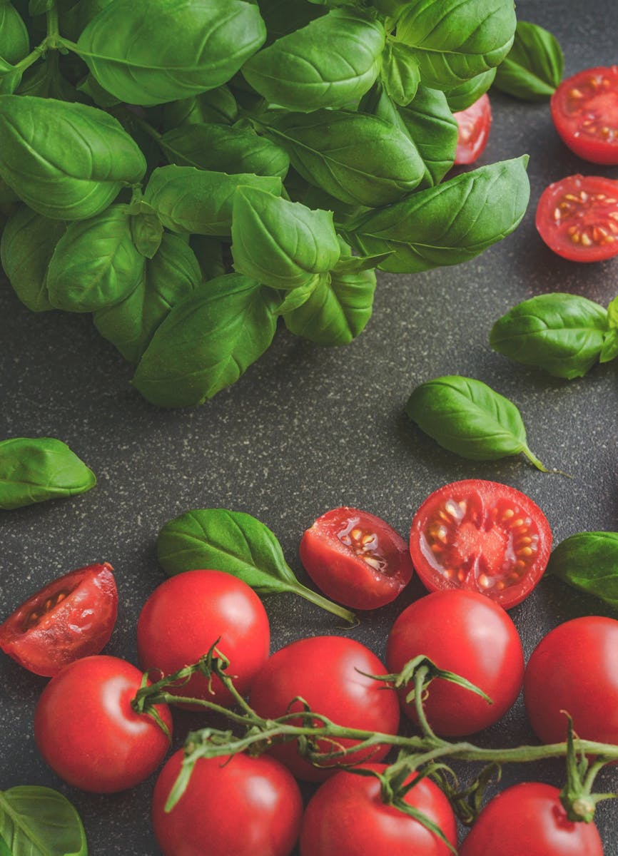 Organic basil leaves with ripe tomatoes on a rustic countertop, highlighting fresh ingredients for cooking.